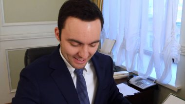 Ofiste masasında evrak okuma ve gülümseyen mutlu genç işadamı portresi