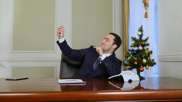 Joven empresario tomando foto selfie con árbol de Año Nuevo utilizando el teléfono celular en la oficina — Foto de Stock