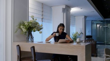 Genç kadın bir kafede kahve yudumlarken dijital tablet kullanma