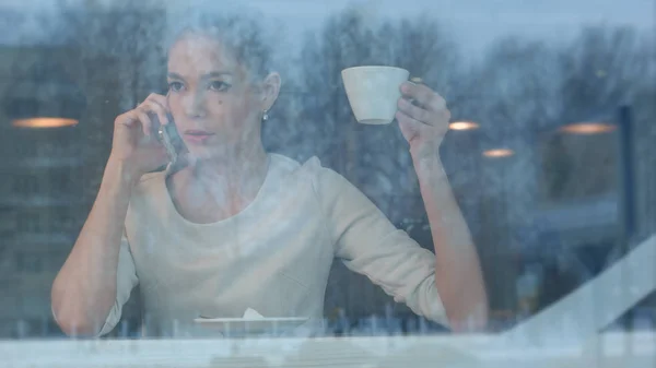 Расстроенная женщина, которая разговаривает по телефону, сидя в кафе — стоковое фото