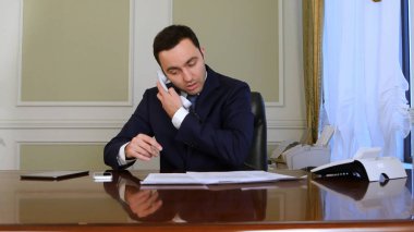 Genç işadamı, bir ofis koltuğunda oturuyorsun, evrak işlerini yapıyor ve telefon görüþmesi Parkinson s hastalığı, saffered devre dışı