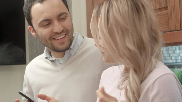 Pareja joven escuchando música a través de un smartphone, hablando en la cocina — Foto de Stock