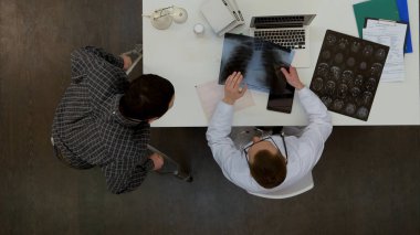 Erkek doktor omurga xray ile erkek hasta koltuk değneği üzerinde tartışıyor.