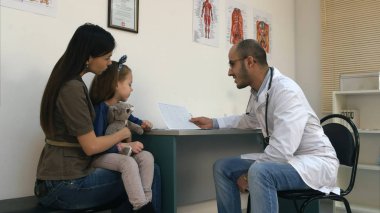 Anne ve küçük kızı kardiyogram açıklayan doktor gülümseyen