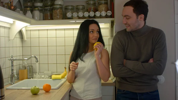 Mujer joven ofreciendo a su novio frutas frescas en su cocina por la noche — Foto de Stock