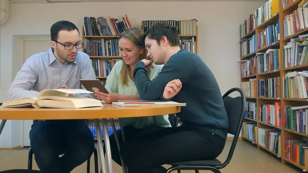 Profesor con grupo de estudiantes trabajando en tableta digital en la biblioteca — Foto de Stock