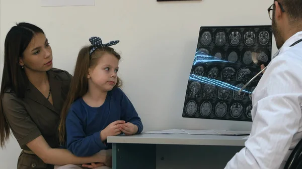 Мужчина врач показывает результаты рентгена мозга счастливой и облегченной женщине с маленькой девочкой Стоковое Фото