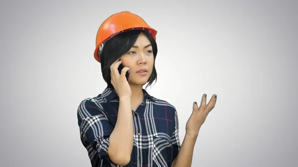 Insinyur wanita dengan helm oranye memiliki panggilan telepon melalui smartphone pada latar belakang putih — Stok Foto