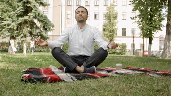 Человек медитирует на зеленой траве в парке с поднятым до небес лицом и закрытыми глазами в солнечный летний день. Концепция медитации, сновидения, благополучия и здорового образа жизни — стоковое фото
