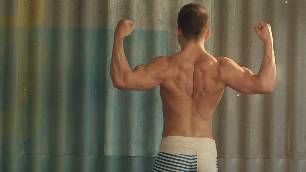 Bodybuilder starker athletischer Muskelmann, Sportler, der seine männlichen Muskeln zeigt, stehender Bac — Stockfoto