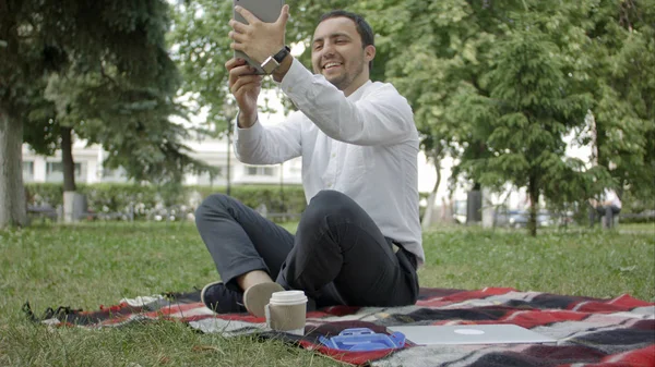 Moderno joven hispano tomando una selfie en el parque, con su tableta . — Foto de Stock