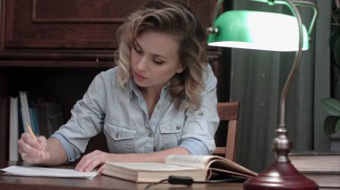 Genç kadın bir kitap ile masaya oturur, yeşil lamba yanar ve çalışmaya başlar