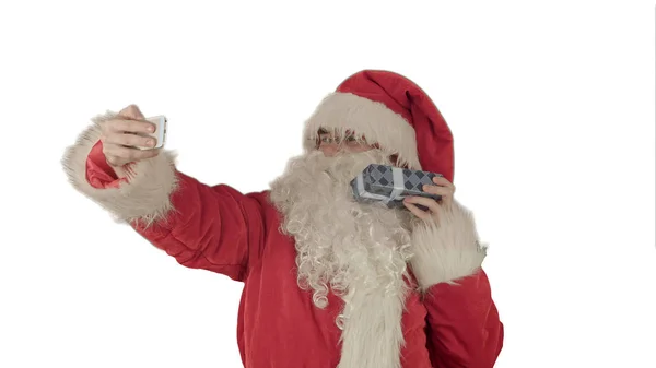 Jultomten som innehar en stor present gör en selfie på smartphone på vit bakgrund — Stockfoto