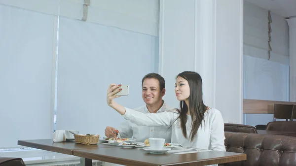 Счастливая молодая пара делает селфи с едой на смартфоне в ресторане — стоковое фото