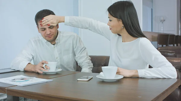 Hombre de negocios enfermo estornudando mientras su compañera preocupada comprueba la temperatura de su cabeza — Foto de Stock