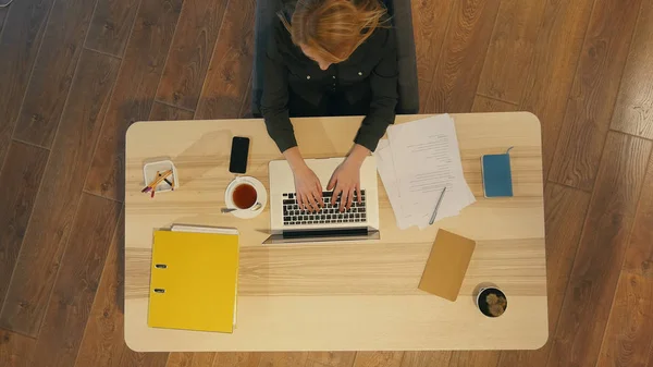 Красивая молодая женщина сидит за столом и печатает на ноутбуке — стоковое фото