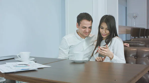 Dos compañeros de oficina en un café mirando sus fotos por teléfono y riendo — Foto de Stock