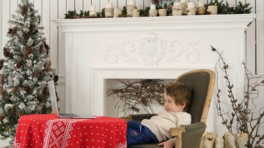 Küçük çocuk Noel ağacı yakınındaki bir dizüstü bilgisayarda Noel Baba'ya mektup yazarak gülümseyen