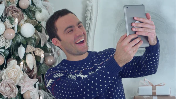 Joven hombre guapo en un jersey de punto de Navidad tomando selfies en una tableta — Foto de Stock