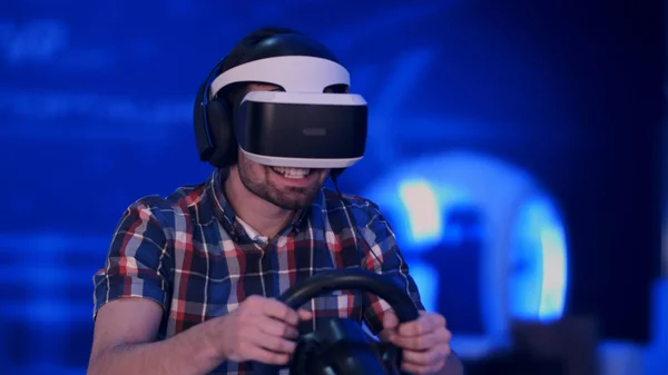 Joven feliz en auriculares de realidad virtual jugando videojuego con rueda de carreras —  Fotos de Stock