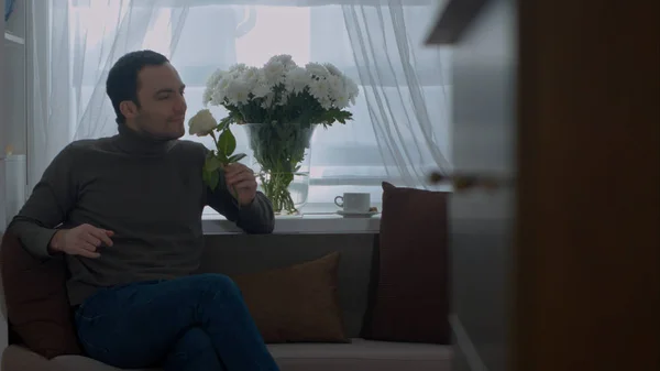 Muž voní růže a snění o jeho ženě v obývacím pokoji — Stock fotografie