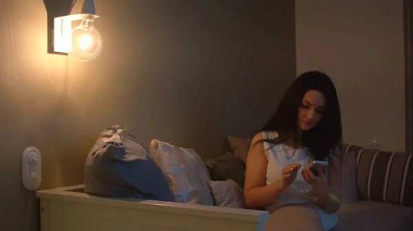 Самотня жінка зі смартфоном чекає когось на дивані вночі — стокове фото