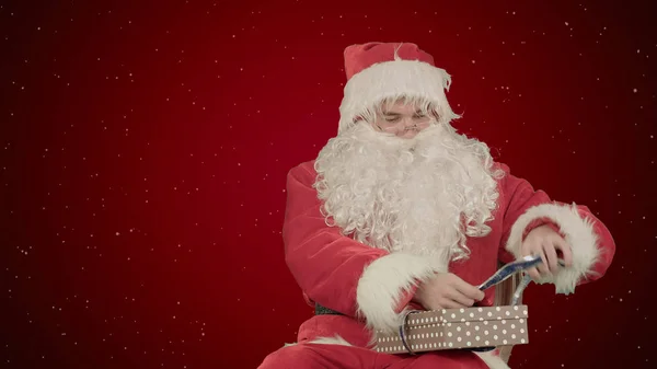 Santa Claus drží vánoční dárky na červeném pozadí se sněhem — Stock fotografie