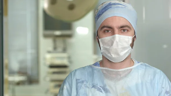 Erfarna unga kirurg, allvarlig man bär ansiktsmask som tittar in i kameran — Stockfoto