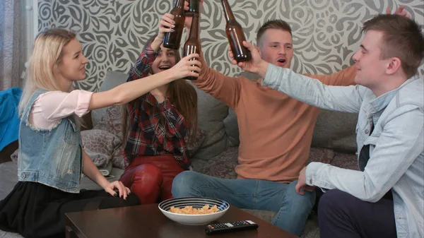 Группа улыбающихся друзей, сидящих на диване и тостующих за бутылку пива — стоковое фото