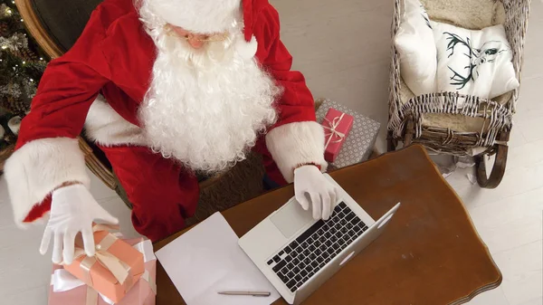 노트북을 사용 하 여 선물을 준비 하는 바쁜 산타 클로스 — 스톡 사진