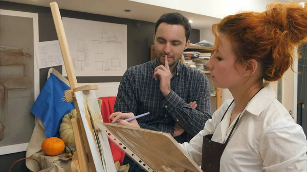 Young male student watching his teacher painting with oil