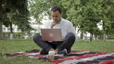 Parlak gün yaz Park'ta dizüstü bilgisayar ile serbest meslek sahibi adam. Casual onun defter üzerinde çalışma ve çim üzerinde oturan adam.