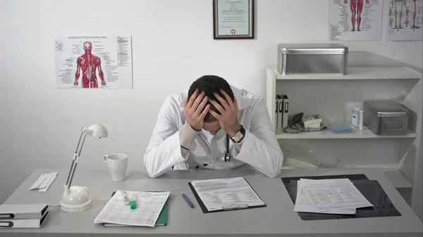 Läkare trött och håller hans huvud på medicinska skåp — Stockfoto