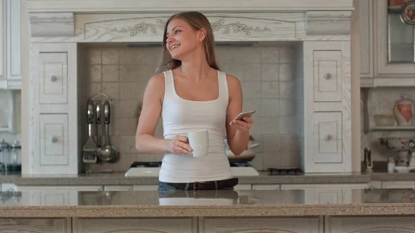 Hermosa mujer joven feliz con teléfono beber café en casa — Foto de Stock