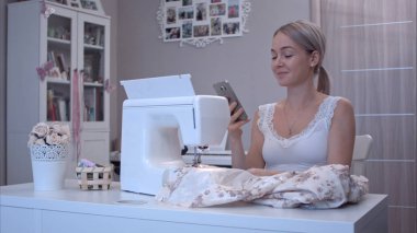 Genç kadın mutlu dikiş makinesi yanındaki masada otururken telefonda konuşurken