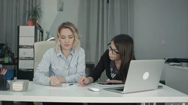 Blonde office woman drawing sketch while brunette coworker suggesting ideas
