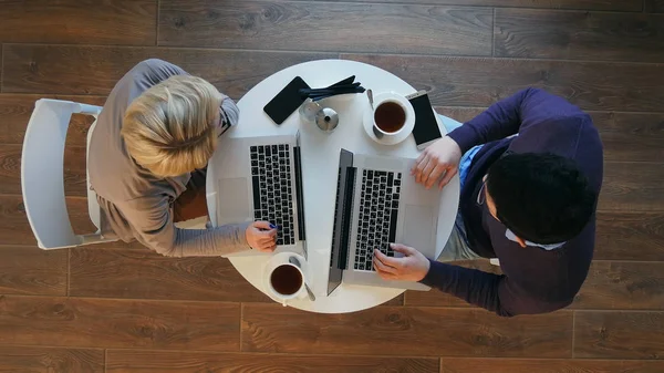 Молодая успешная деловая пара обсуждает документы, пьет кофе и улыбается во время работы в кафе — стоковое фото