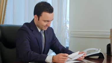 Ofiste masasında evrak okuma ve gülümseyen genç işadamı