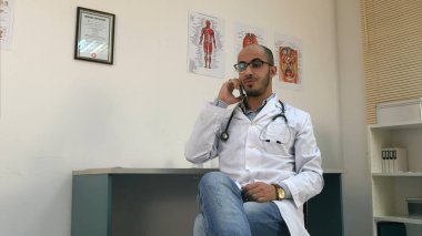 Cep telefonu üzerinde konuşurken ve bakarak genç erkek doktor