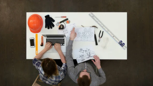 Arquitecto trabajando en planos mientras colega escribiendo en el portátil — Foto de Stock