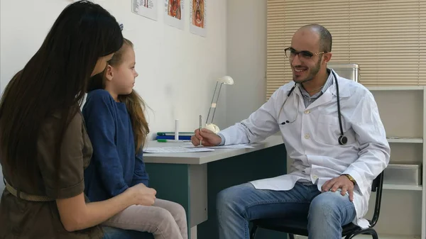 彼女の母親の周上に座って内気な少女と話している男性医師の笑顔 — ストック写真
