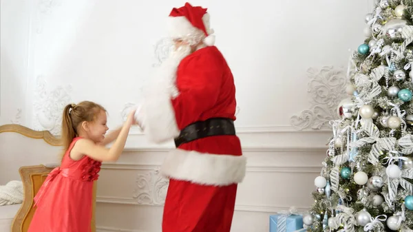 Linda niña bailando junto a Santa Claus junto al árbol de Navidad —  Fotos de Stock