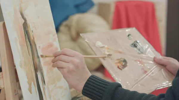 Manos de artista masculino aplicando pinceladas sobre lienzo y sosteniendo paleta — Foto de Stock