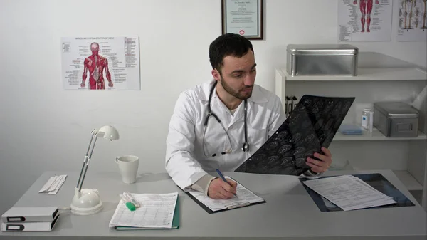 Medical doctor sitting at table and positively exploring patients brain mri — Stock Photo, Image