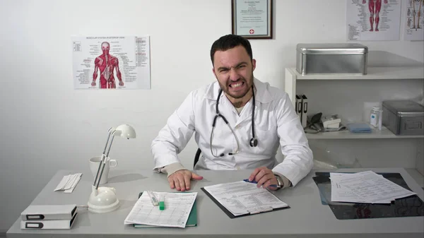 An angry doctor slamming his fist on the desk in front of him.