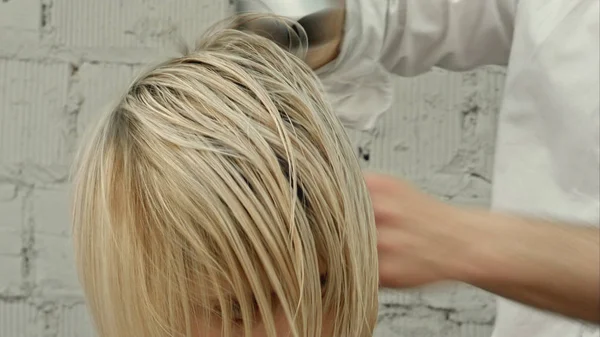 Penata rambut mengeringkan rambut wanita menggunakan pengering rambut — Stok Foto