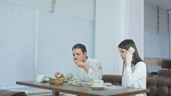 Молодой человек ест, пока его девушка разговаривает по телефону в ресторане — стоковое фото