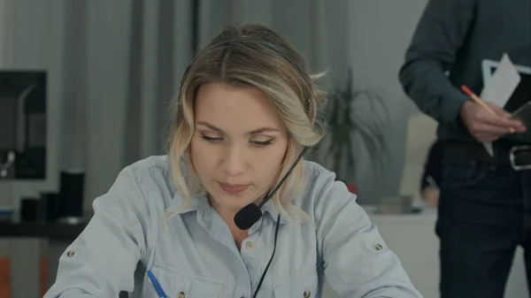 Tired woman in office stretching her neck while her boss putting laptop at her desk