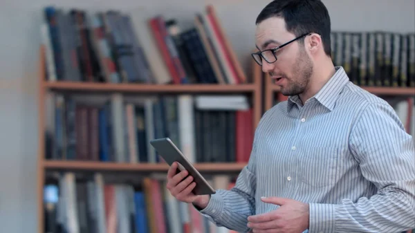 Jeune professeur masculin visioconférence sur tablette à la bibliothèque — Photo