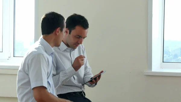 Два бизнес-руководителя сидят в светлом офисе и ищут информацию вместе, делясь экраном цифрового планшета — стоковое фото